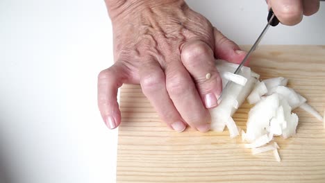 caucasian person with old hands, cutting onion, on a wooden board