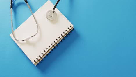 video of stethoscope on notebook, on blue background with copy space