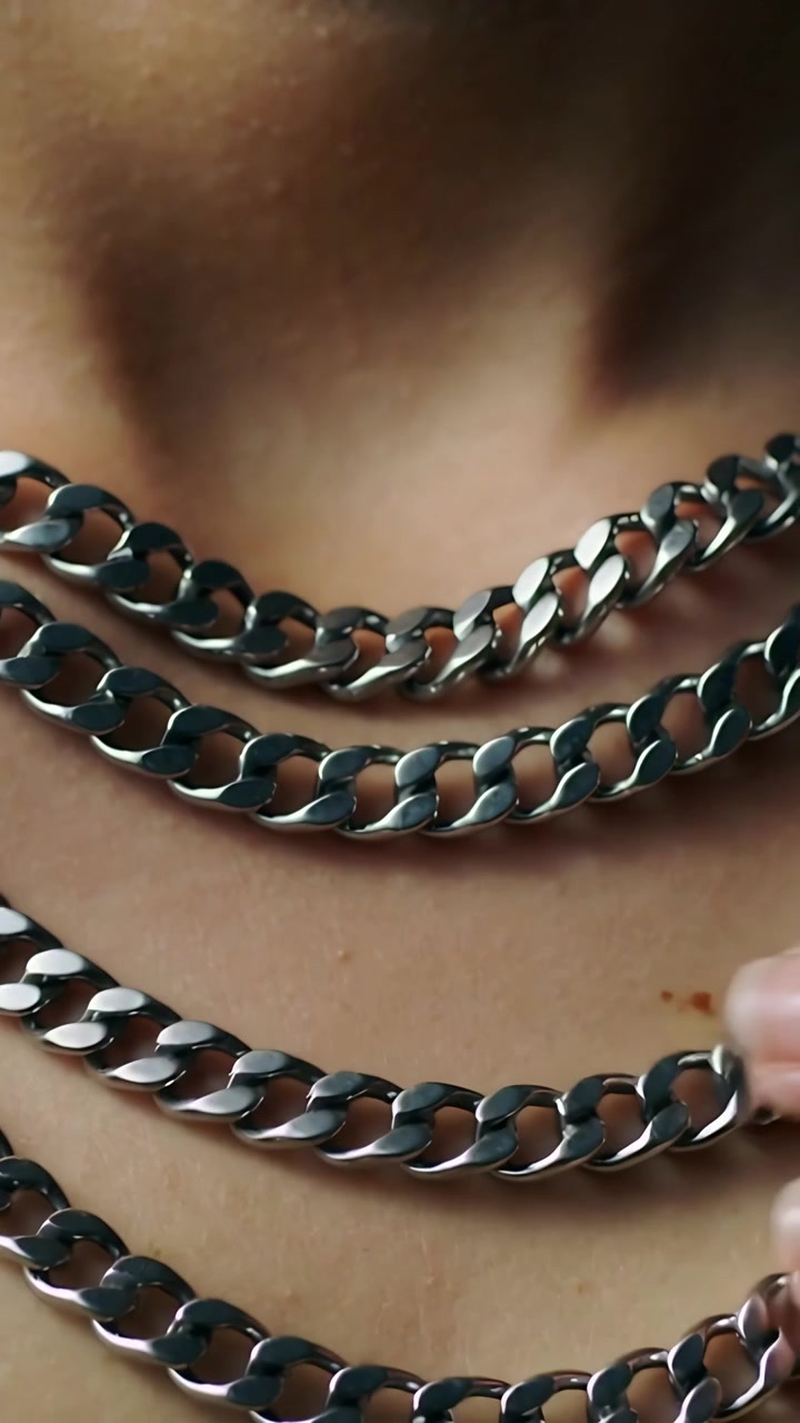 Vertical video: Entering hand arranging three silver chains on neck in closeup, aligning layers
