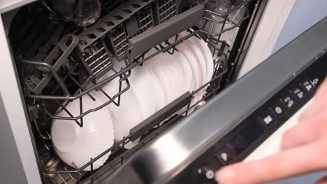a woman is choosing a dishwashing program on a dishwasher builtin