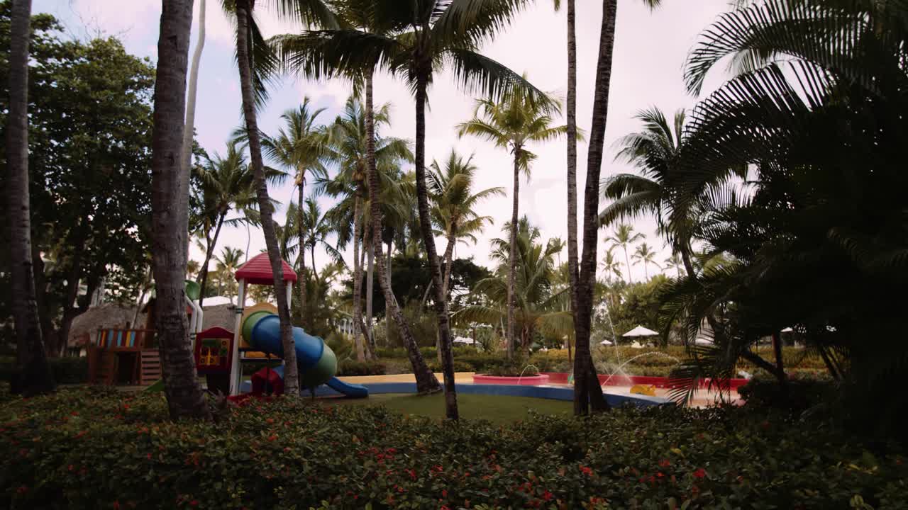 Colorful kids play zone amongst palm trees in tropical resort; slomo