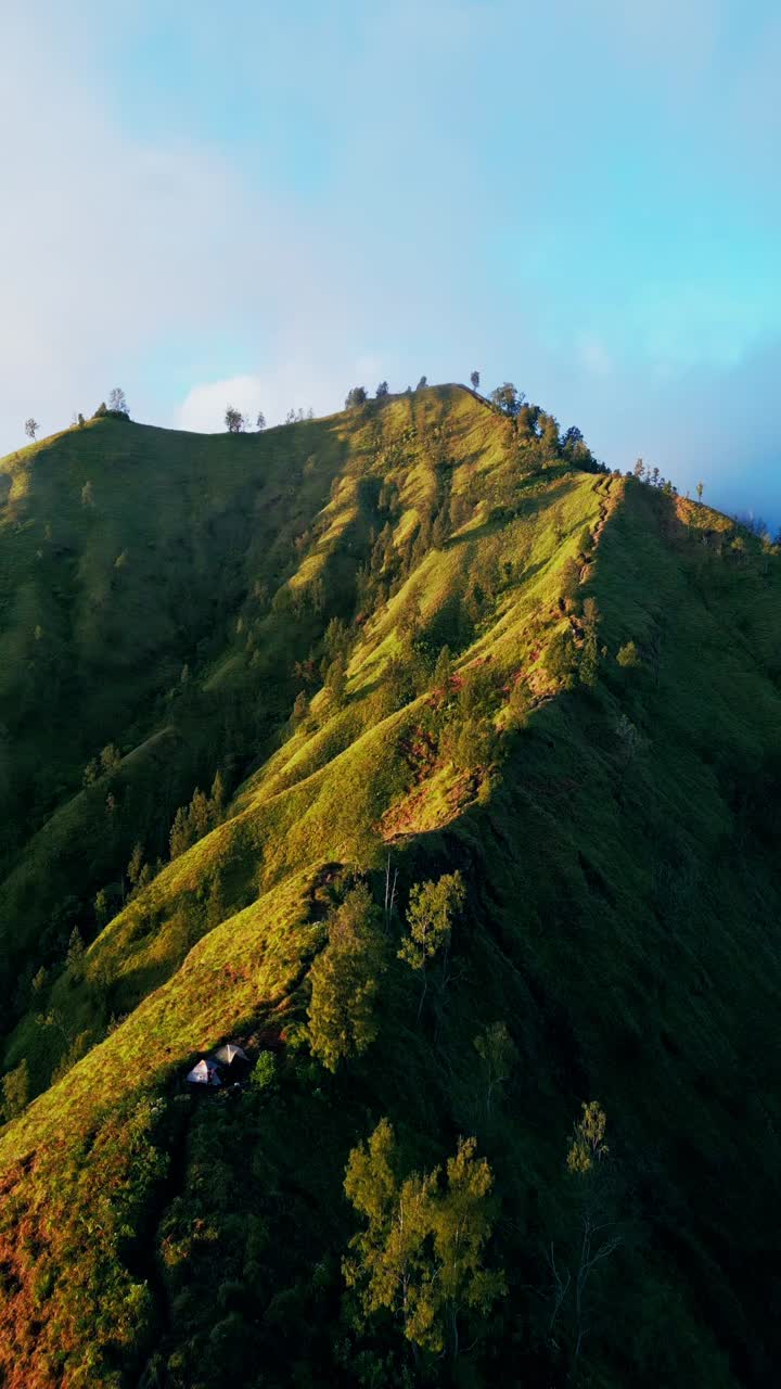 Video vertikal merekam matahari terbit keemasan yang menakjubkan di atas Bukit Trunyan di Bali, menyoroti suasana berkemah yang tenang, pemandangan gunung yang dramatis, dan lingkungan alam yang damai