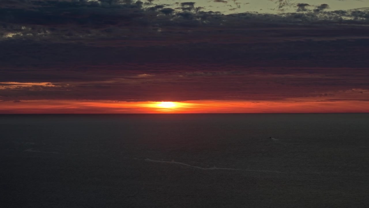 Eine Teleobjektiv-Luftaufnahme des Sonnenuntergangs, mit glühenden Wolken darüber und dem Horizont, der vom Pazifischen Ozean vor der Küste von Los Cabos, Baja California, Mexiko, markiert wird.