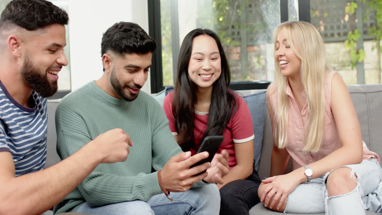 Friends sitting on couch, smiling and looking at smartphone together