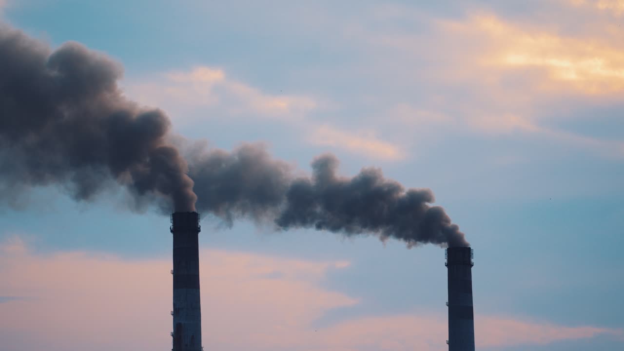 Two pipes with thick dirty smoke filling the air. Large pipes with dark fumes is poured from the factory pipes on the evening sky. Pollution of the environment.