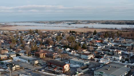 Slow-aerial-dolly-left-shot-of-snow-covered-town-of-Thurso-Quebec-Canada-with-the-frozen-Ottawa-River-visible-in-background-on-a-winter-day