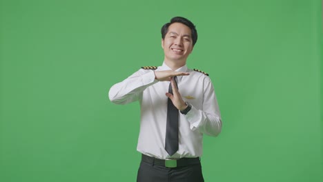 아시아 남성 조종사가 카메라를 바라보고 시간을 보여줍니다. 녹색 화면 배경 스튜디오에 서있는 동안 손 제스처
