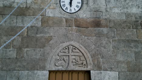 heavy wooden doors with stone coat of arms and clock with bell tower on outside of church