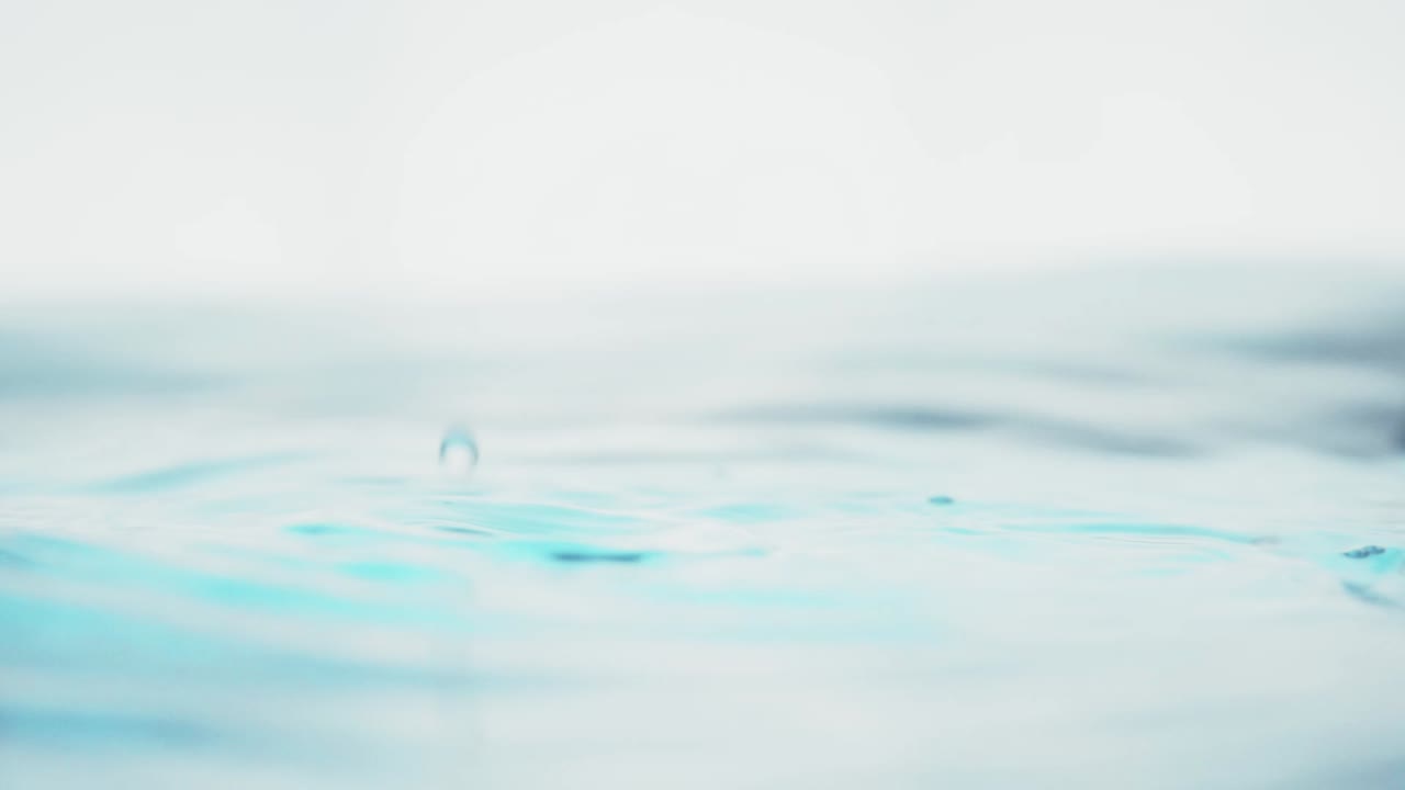 The clean water surface in slow motion fills the screen with water splashing shop the water drop and waving liquid surface with an air bubble