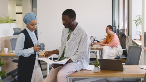 muslim businesswoman talks to a young worker who is holding a notebook and is leaning on his desk