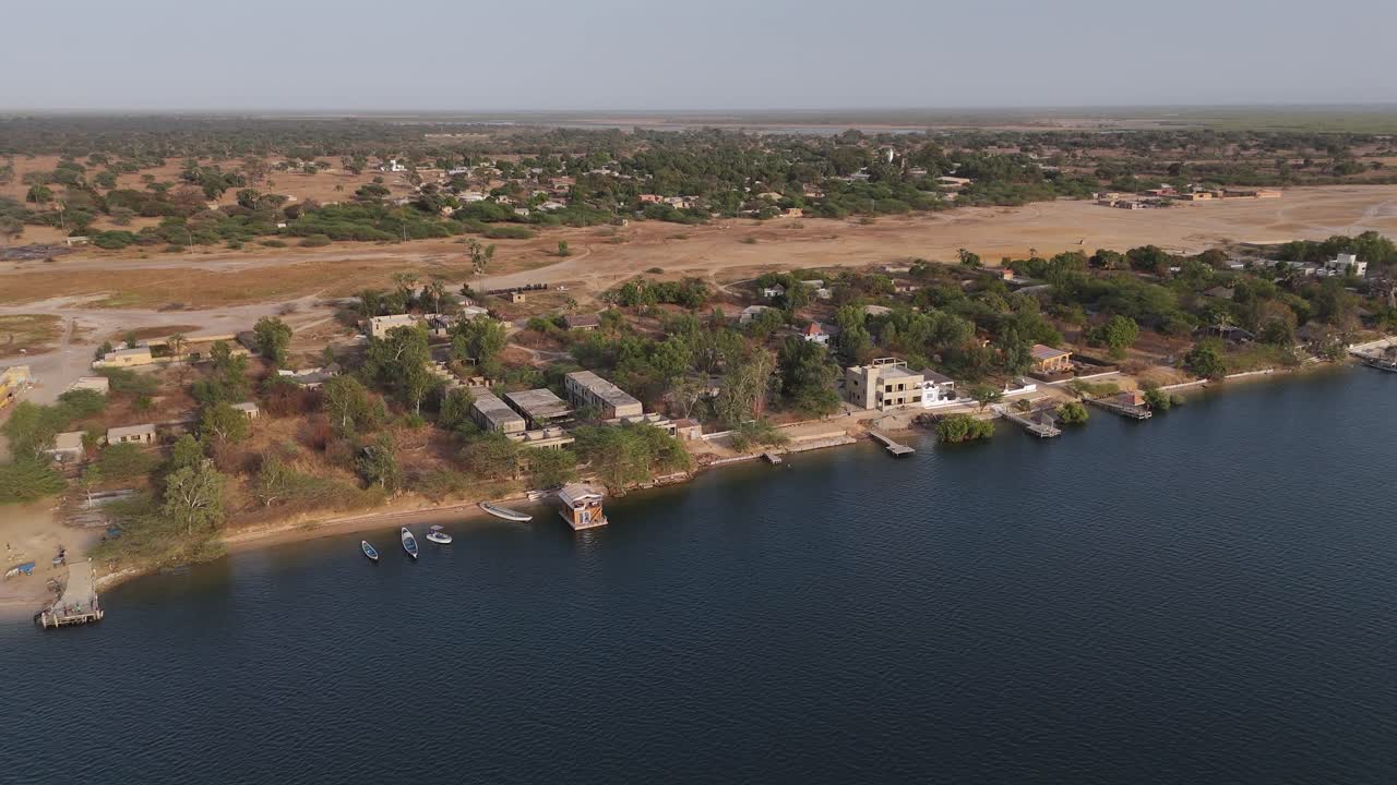 Aerial drone footage of a riverside village in Sine Saloum Delta, Senegal. Scenic view of houses, boats and shoreline blending into vast natural landscape