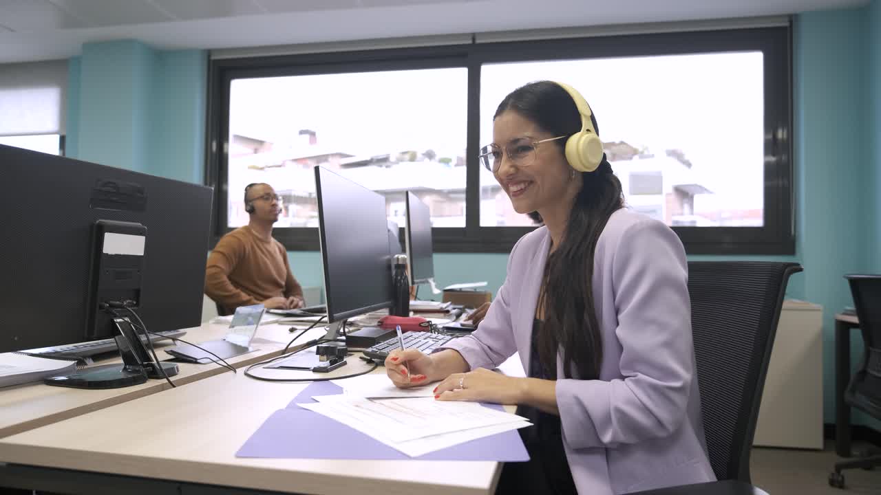 Happy businesswoman looking away while writing on documents at desk in creative office