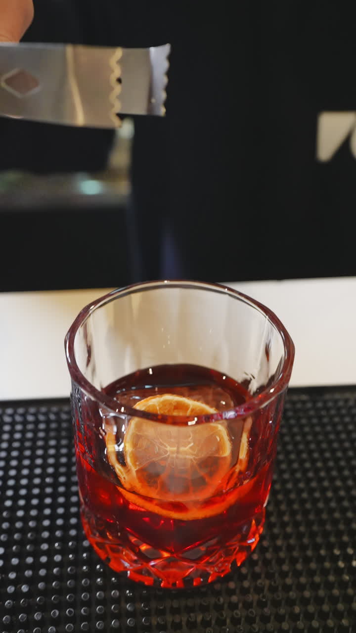 Barman che fiammeggia una guarnizione di arancia su un cocktail rosso