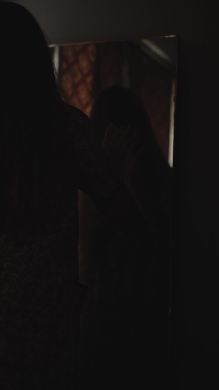 Dark and moody vertical Halloween horror scene featuring a creepy woman gazing into a cracked mirror inside an abandoned haunted room. Perfect for spooky intros, thriller trailers,