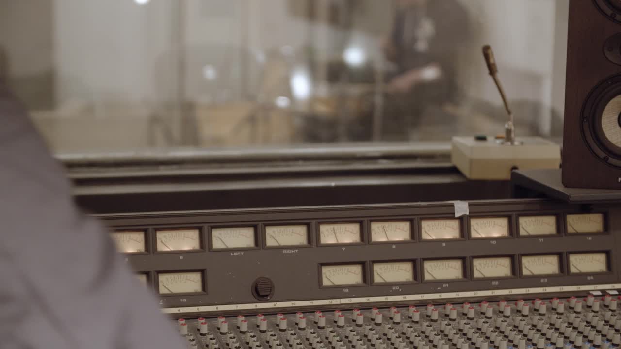 Recording studio - Vintage recording desk with engineer adjusting settings - drummer in background playing