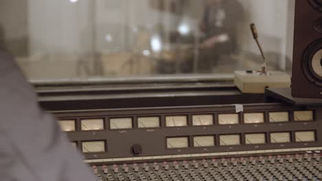recording studio - vintage recording desk with engineer adjusting settings - drummer in background playing