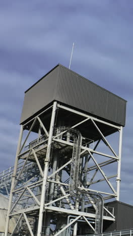 high metal construction standing next to the elevator tanks. looking at the tops of modern granary buildings at the backdrop of grey cloudy sky. vertical video