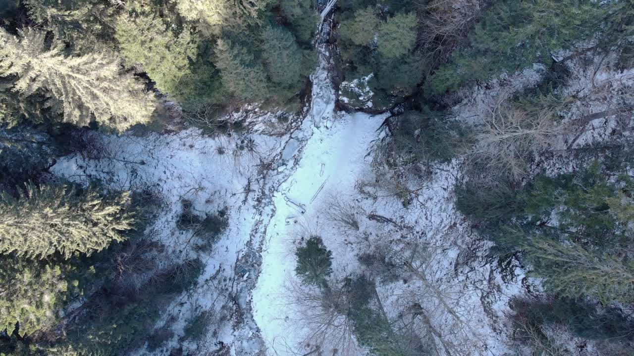 drone asciende en montañas de bosque cubiertas de nieve con río helado