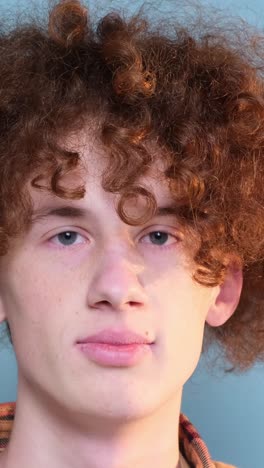 a guy with curly hair is looking at the camera on a blue background in the studio a guy with curly hair is looking at the camera on a blue background in the studio