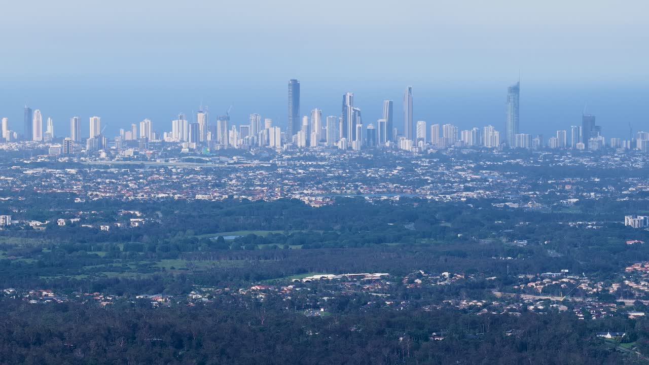 Wide aerial pan reveals Gold Coast skyline, suburban housing, and hinterland under soft daylight
