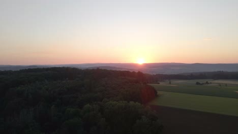 bird's eye view at sunset of meadows and cornfields in a valley surrounded by forests