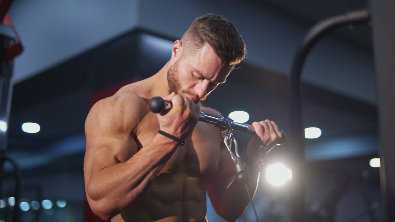 Bodybuilder pumping arm muscles. Handsome guy with muscular body doing his daily workout to improve his muscles in the gym. Close-up.