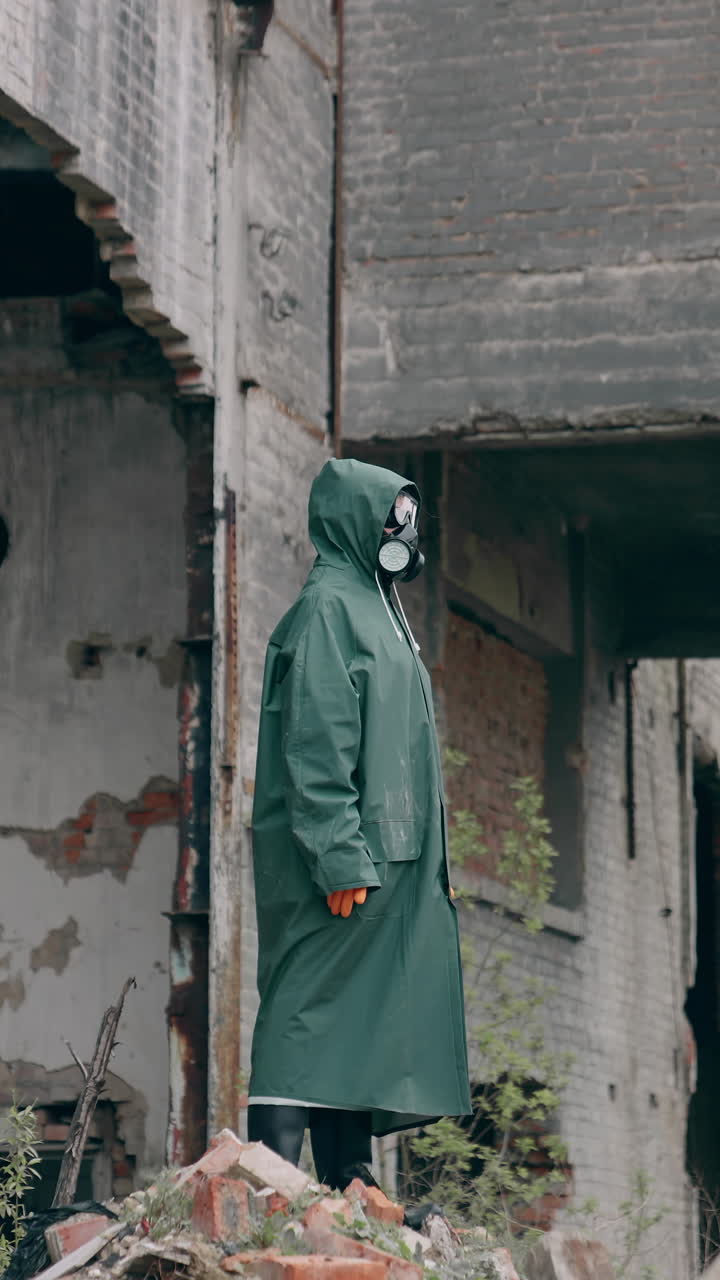 Survivor in abandoned place with radiation. Virologist man in protective costume and respirator gas mask stands in a deserted industrial factory background. Vertical video