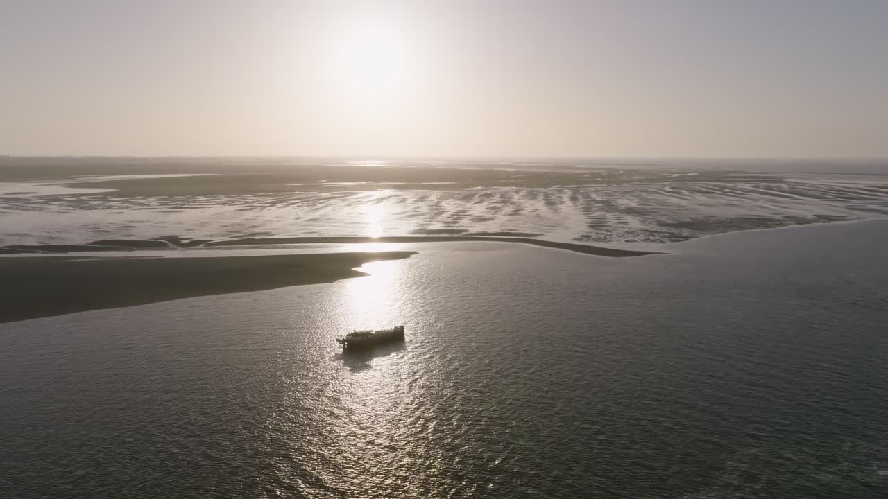 Calm morning scene with a luxemotor boat on open water next to expansive Wadden sea mudflats areas and distant sandbars