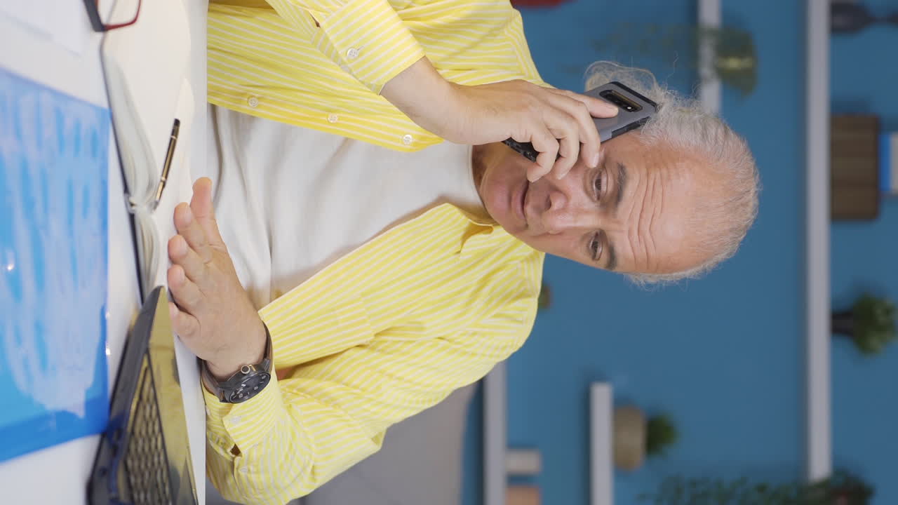 홈 오피스 근로자의 수직 비디오  ⁇ 은이가 오래된 관리 자격으로 전화로 이야기합니다.