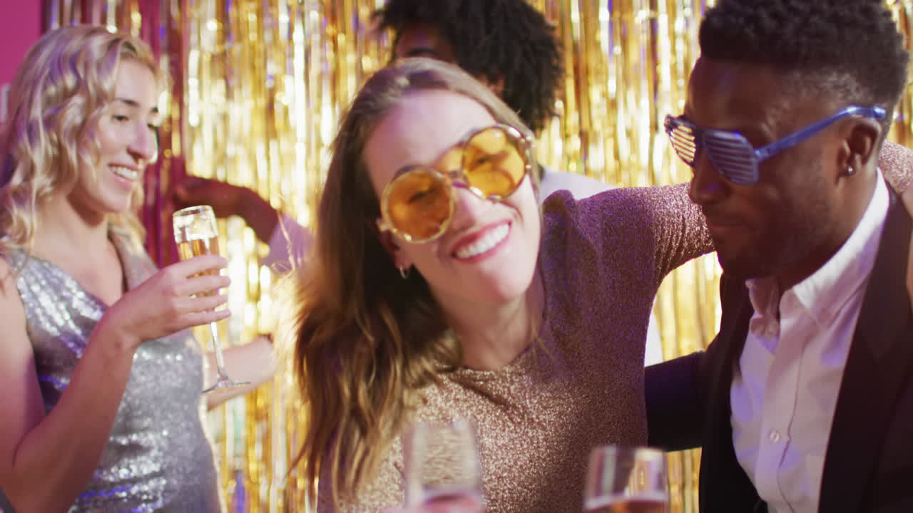 Video of two happy diverse couples dancing holding glasses of champagne at a nightclub