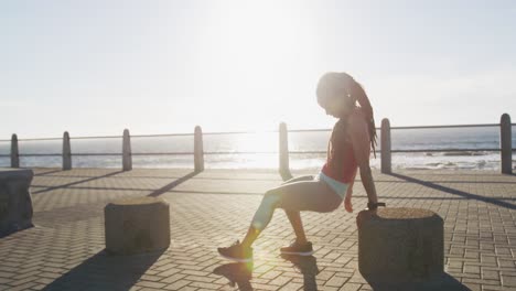 african american woman in sportswear exercising on promenade by the sea