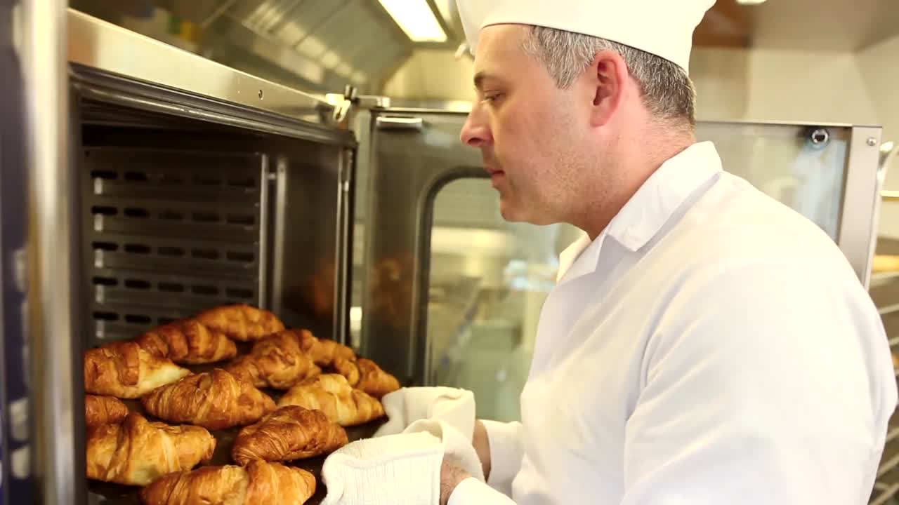 Smiling baker taking fresh croissants out of the oven