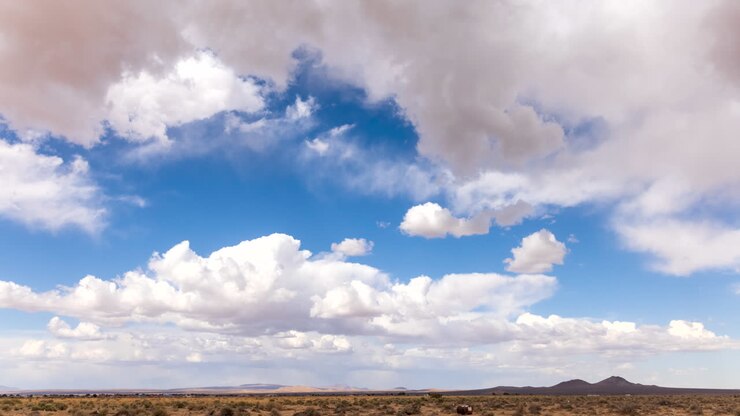 Nubes con formas abstractas cruzan el cielo azul sobre la tierra árida del desierto de Mojave - lapso de tiempo estático.