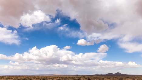 clouds in abstract shapes blow across the blue sky over the barren land of the mojave desert - static time lapse