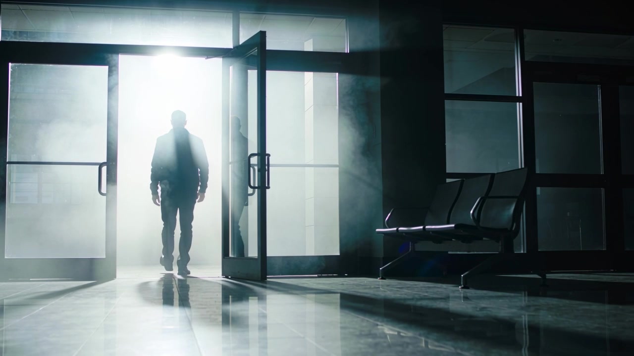 Walking man in dark coat moving through open left glass double doors into lobby, backlit haze