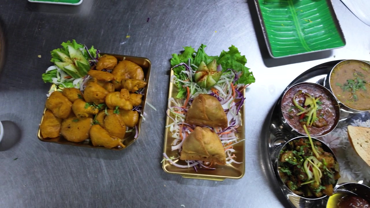 Una telecamera dall'alto panoramica su una varietà di piatti indiani inclusi thali, samosa e pakora.