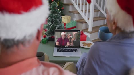 Happy-caucasian-senior-couple-on-video-call-on-laptop-with-adult-children-at-christmas-time