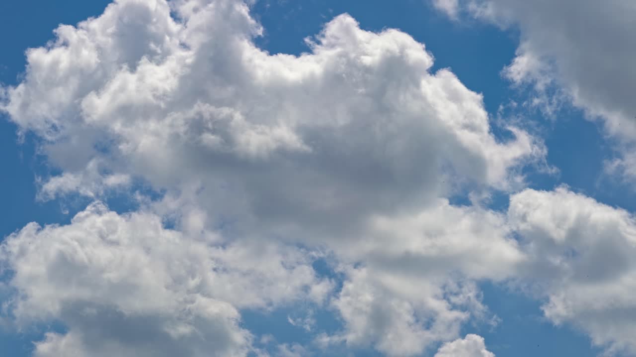 Fluffy clouds float across a bright blue sky on a sunny day