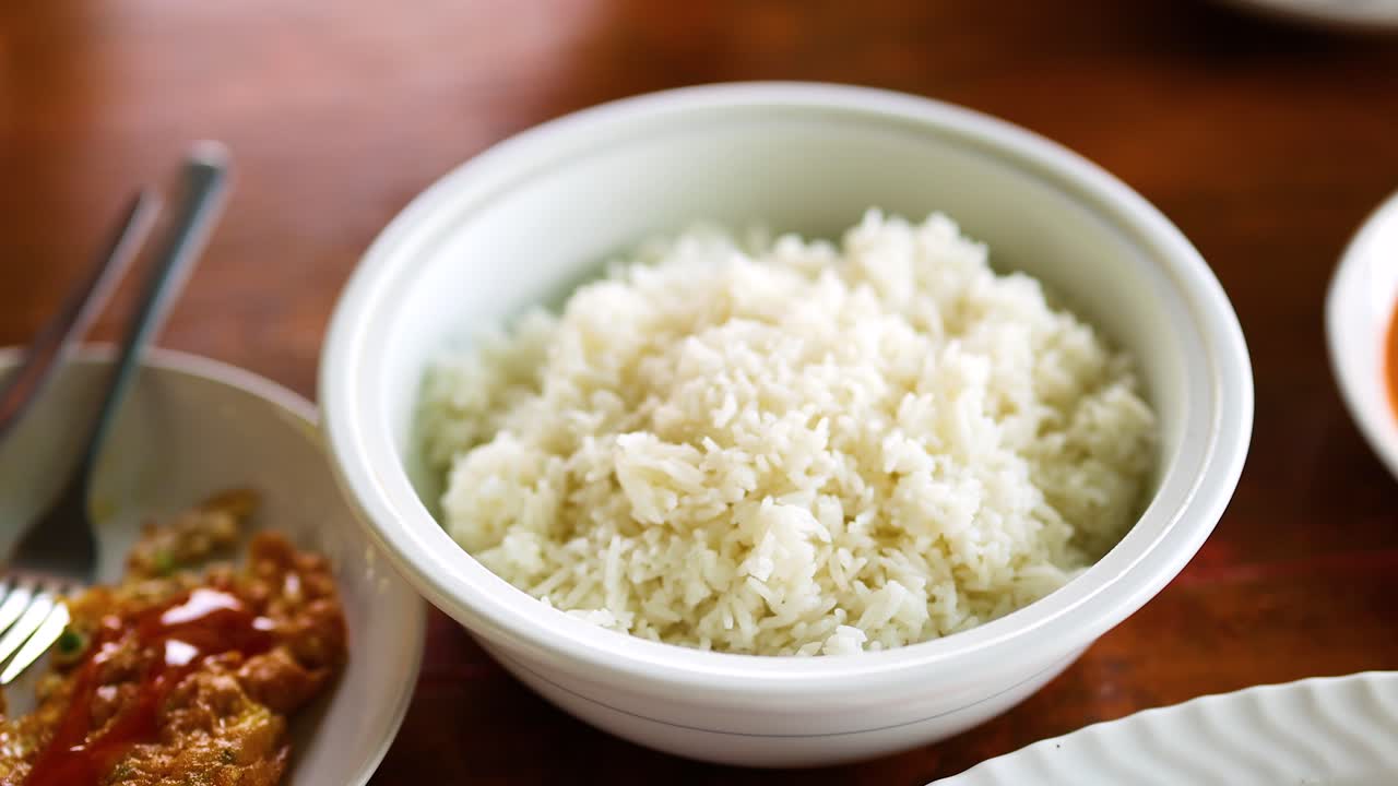 una mano abre un plato de arroz en una mesa de madera, revelando arroz recién cocido junto a un plato con salsa