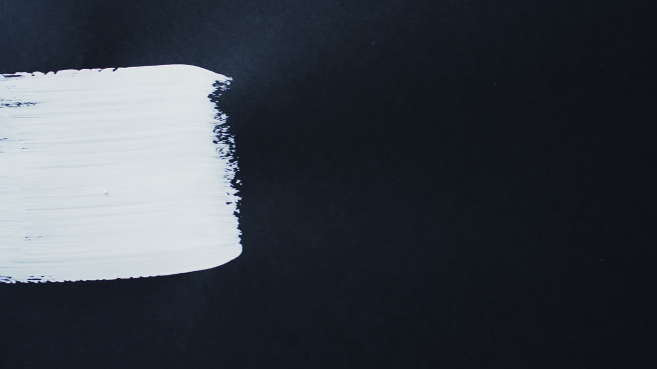 близкое изображение белой полосы краски на черном фоне с копировальным пространством, замедленное движение