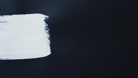 close up of white paint stripe on black background with copy space, slow motion