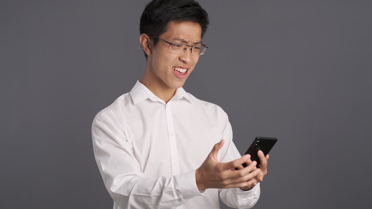 Uomo asiatico che usa lo smartphone e si arrabbia