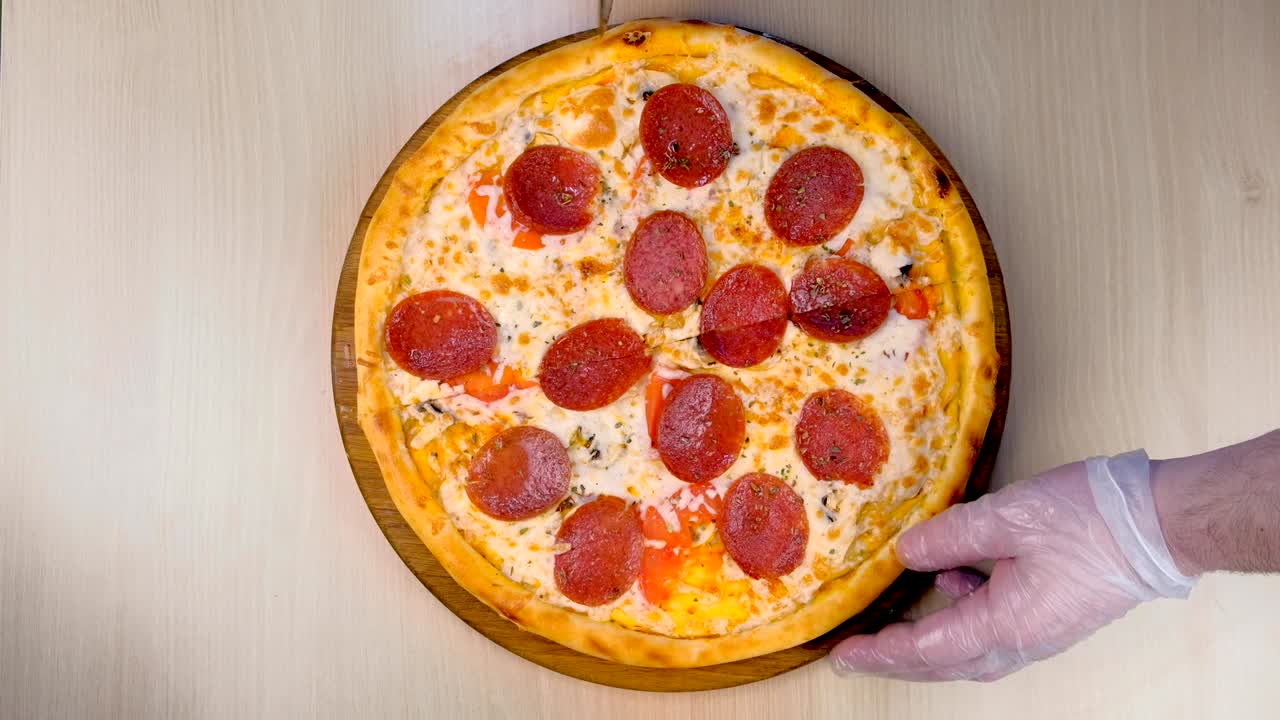 요리사는 살라미 피자를 조각으로 잘라줍니다. 고무 장갑을 입은 손으로 가까운 위쪽을 보세요.