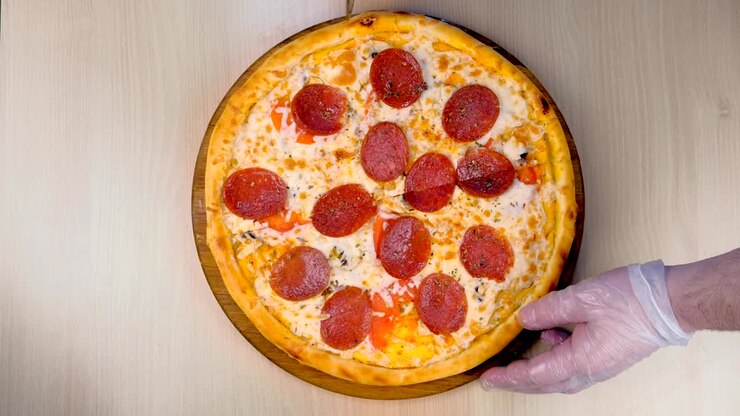 Un cuoco taglia la pizza al salame a fette. Mani con guanti di gomma, vista dall'alto ravvicinata
