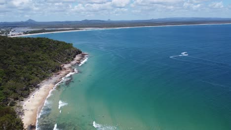 aerial view of a peninsula with sandy beach, rocky beach and surfers below