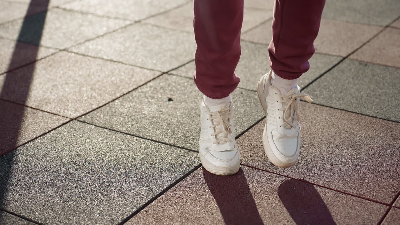 Sport woman in white sneakers jogs across sunlit textured tiles casting bold shadows under clear sky in outdoor urban playground setting, highlighting footwork, and energy in fitness warm up routine