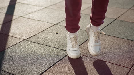 sport woman in white sneakers jogs across sunlit textured tiles casting bold shadows under clear sky in outdoor urban playground setting, highlighting footwork, and energy in fitness warm up routine
