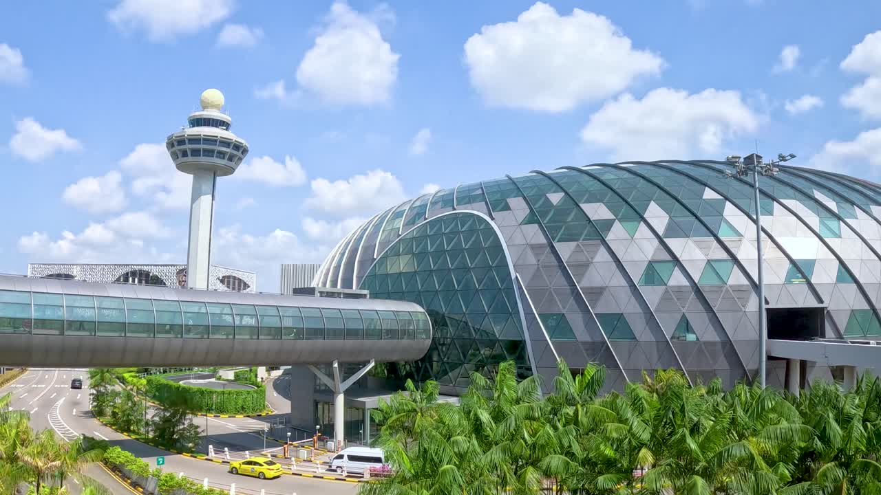 Camera pans across futuristic glass terminal, lush greenery, and control tower under bright daylight