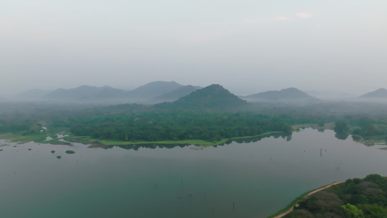 Golden sun over misty forests and distant hills beside open water in Sri Lanka