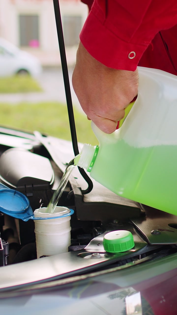 Service worker man pours car fluid windscreen green cleaning washer glass summer or winter cleaner